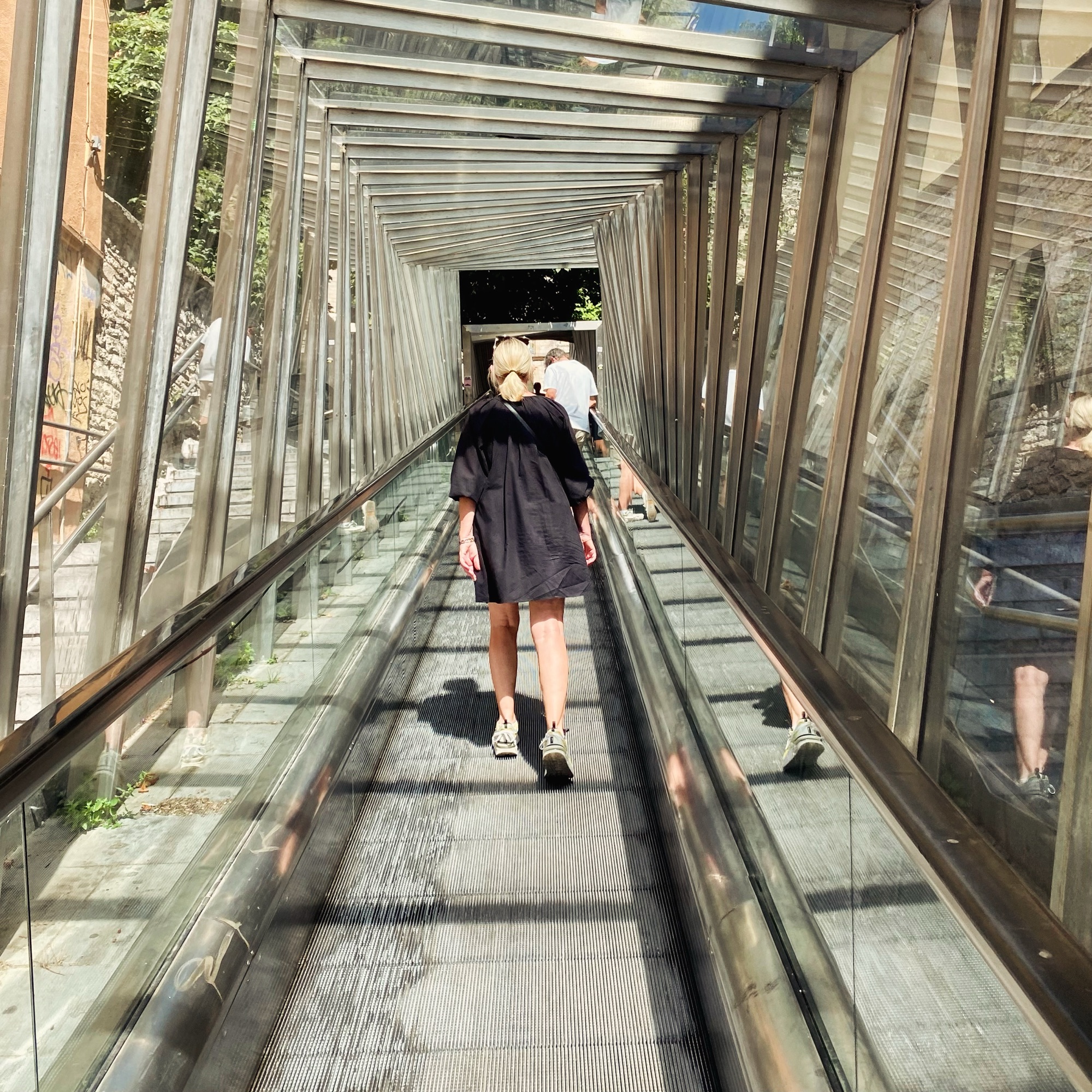 A woman in a black dress rides an escalator through a glass tunnel with other visitors on the way to the cathedral.