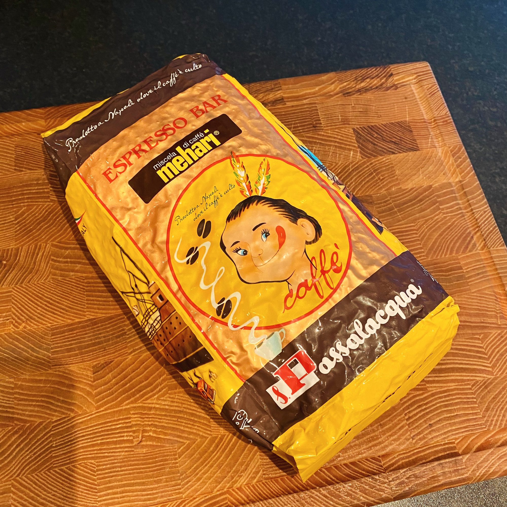 A yellow and brown Passalacqua Mehari espresso coffee bag rests on a wooden board, with vintage face artwork.