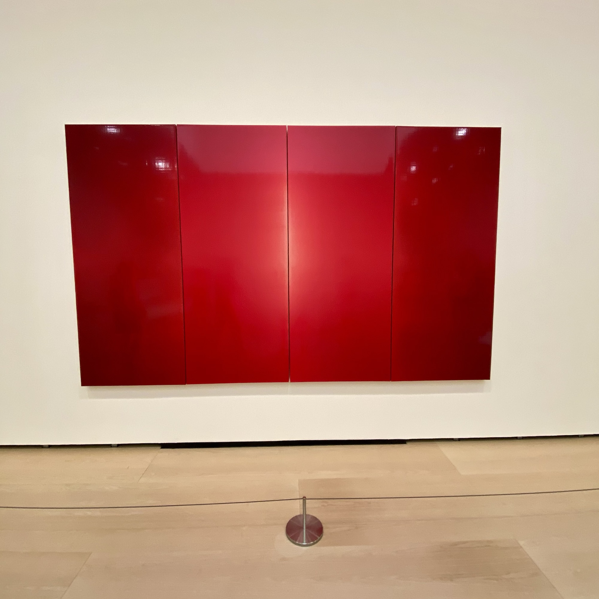 Four glossy red panels by Prudencio Irazabal stand on a white wall, with layered colour glowing under gallery light.