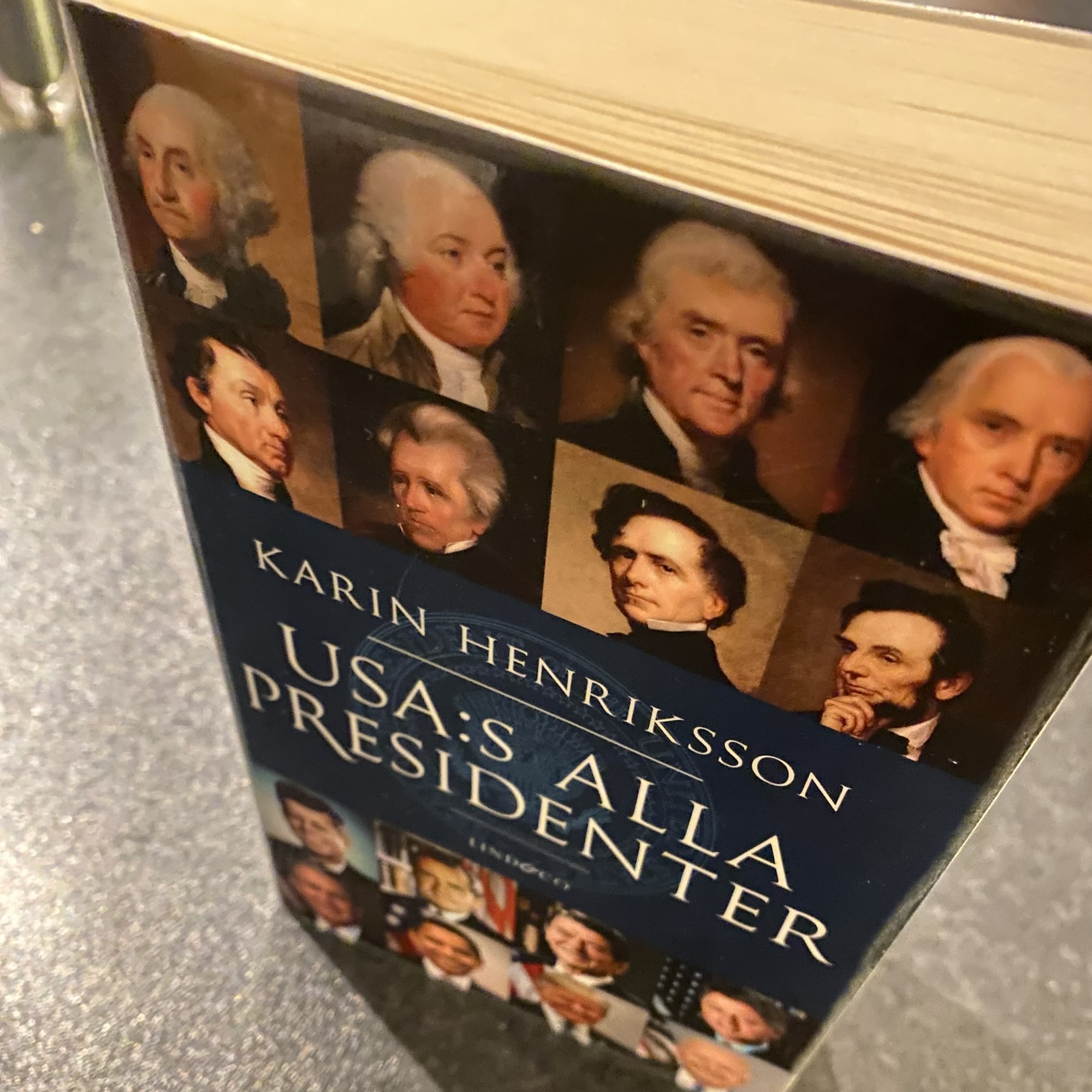 A blue-covered book by Karin Henriksson, USA:s presidenter, displays painted portraits of several US presidents.