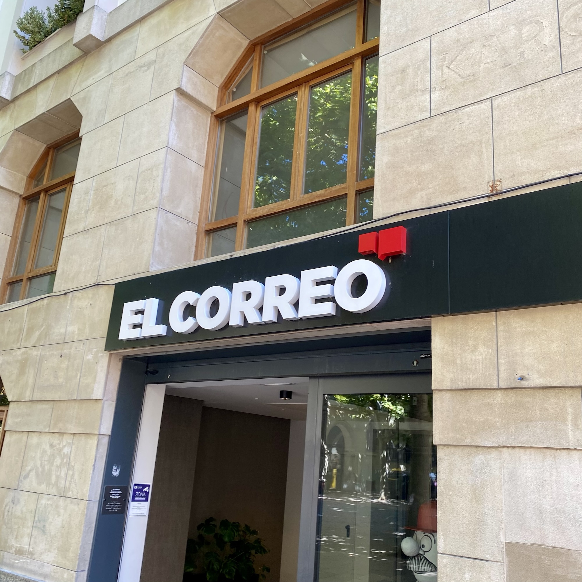 EL CORREO signage stands out on a stone building façade with tall wooden windows and a glass doorway below.