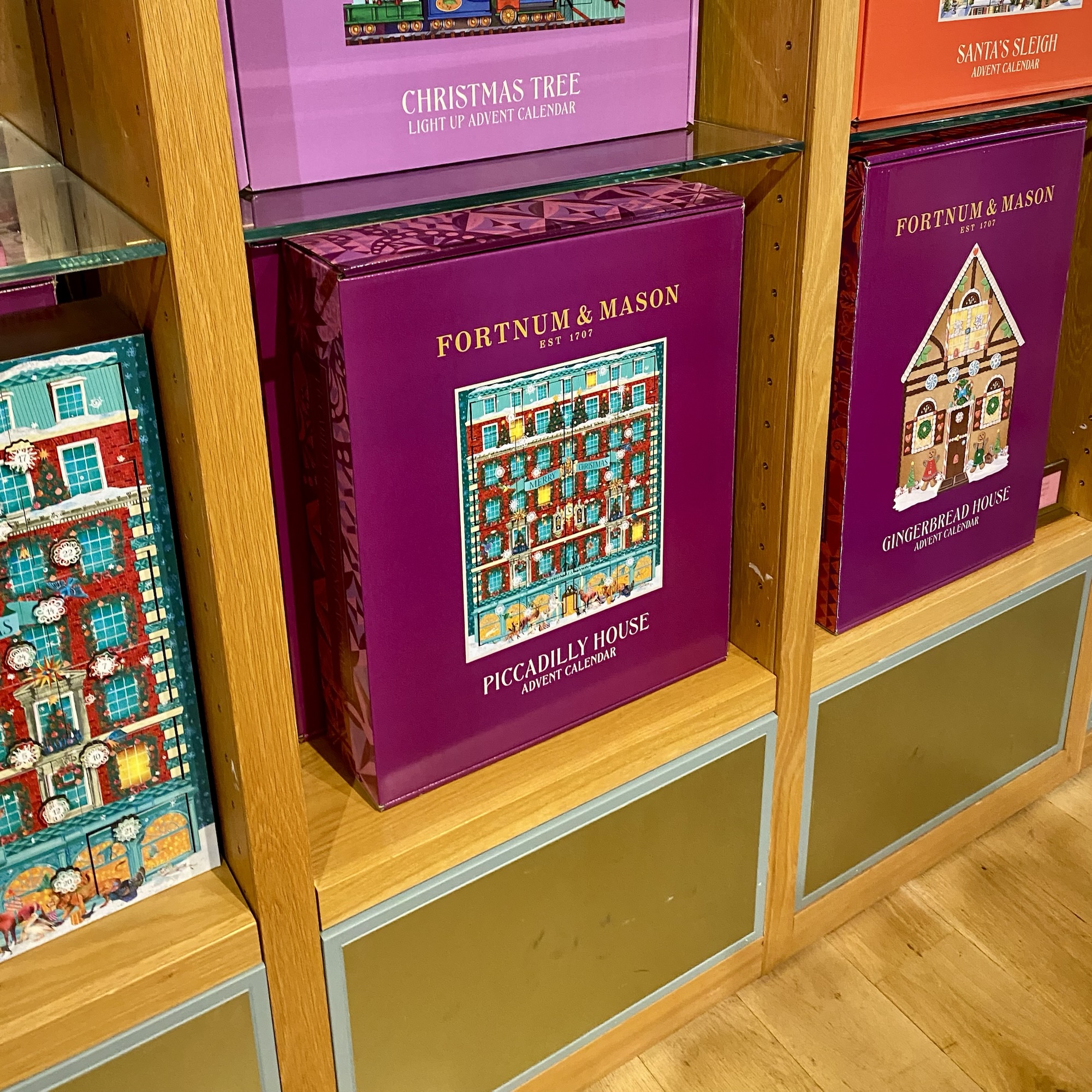 Colourful Fortnum & Mason advent calendars, including Piccadilly House and Gingerbread House designs, on wooden shelves