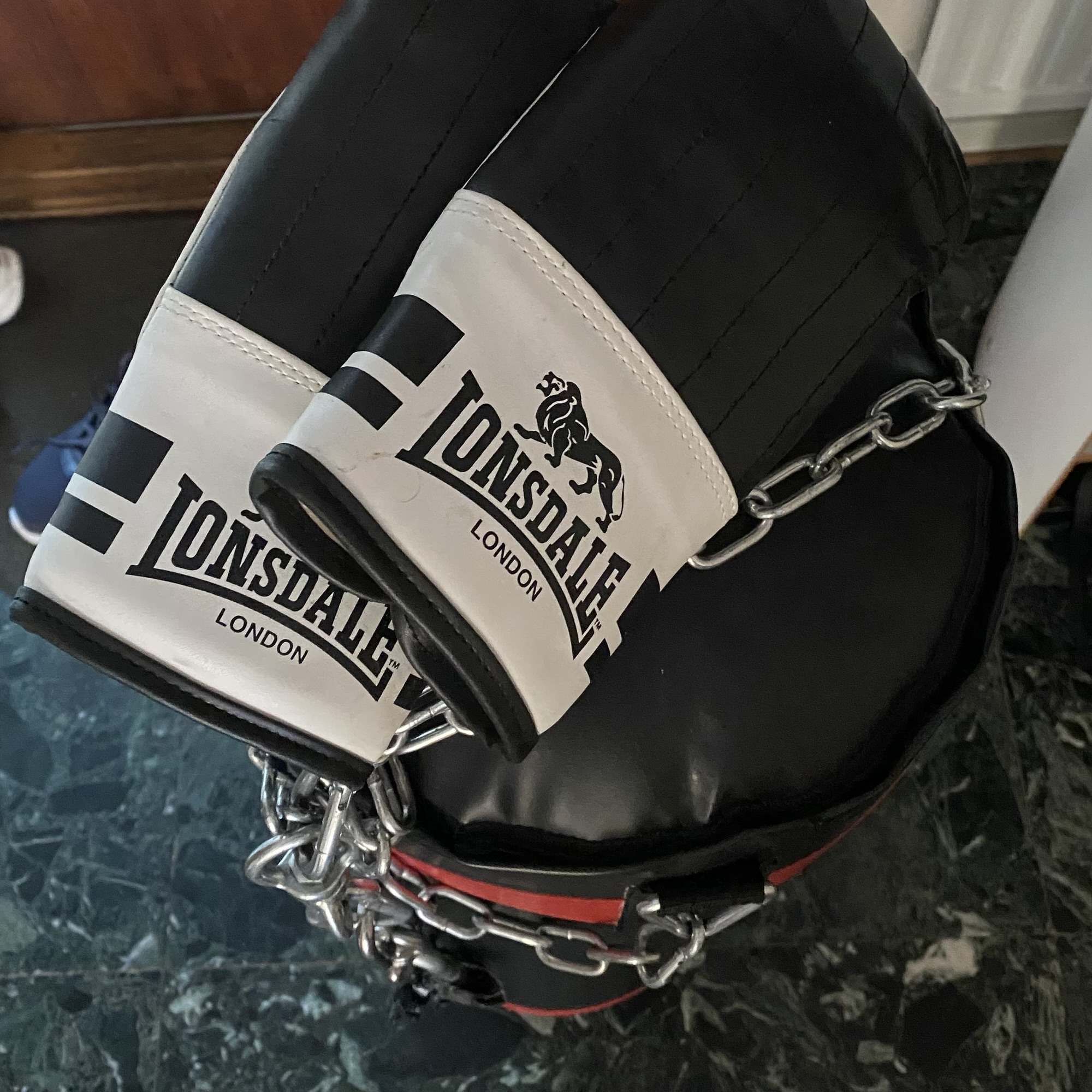 A chained black heavy bag with white Lonsdale London straps stands ready for a Friday boxing session and combination practice.